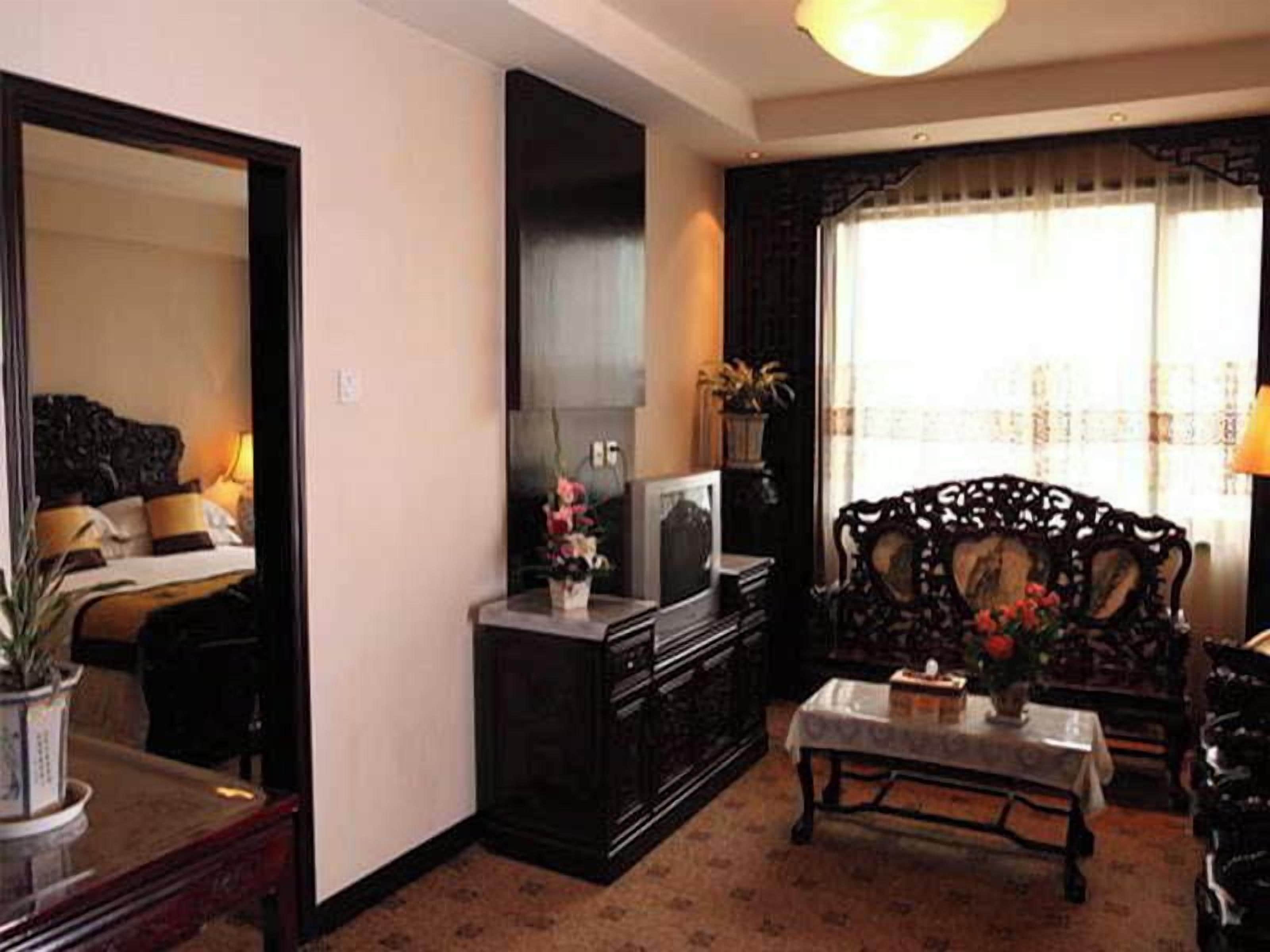 A hotel room with a bed, a television, a sofa, a table, and a window with curtains.
