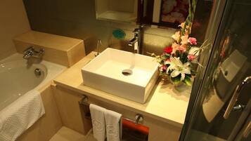 A bathroom with a bathtub, a sink, and a shower. There is a towel rack with towels and a decorative flower arrangement.