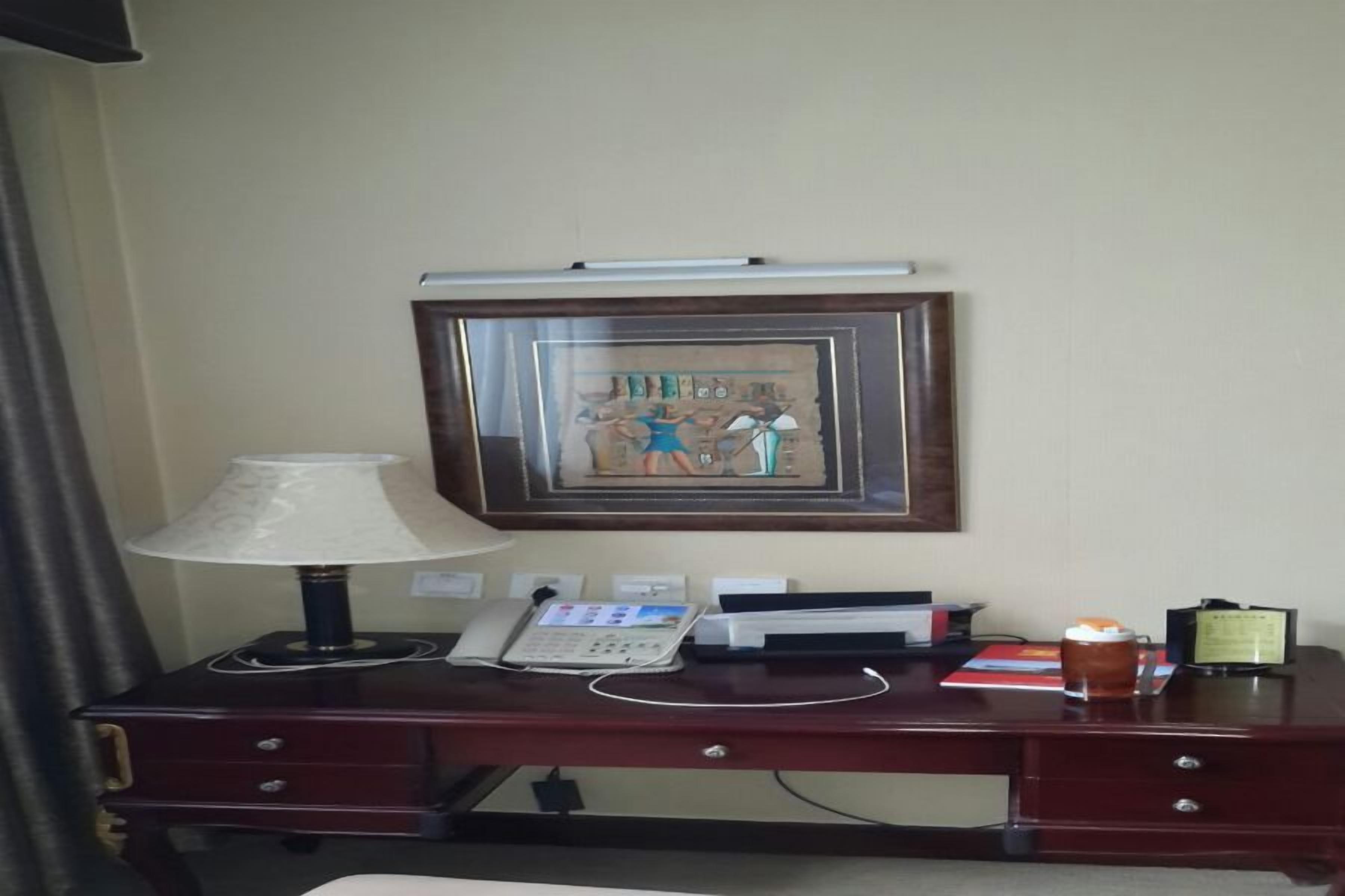 A hotel room desk with a lamp, phone, and framed artwork on the wall.