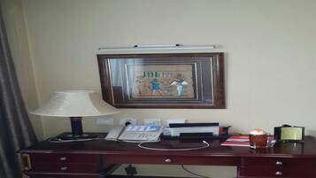 A hotel room desk with a lamp, phone, and framed artwork on the wall.