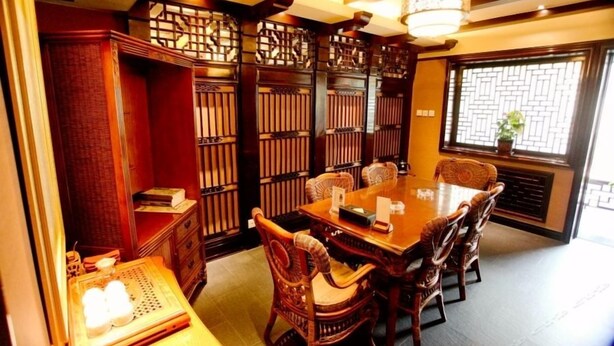 Un salón de reuniones de estilo tradicional con una mesa y sillas de madera, un biombo decorativo y una lámpara colgante.