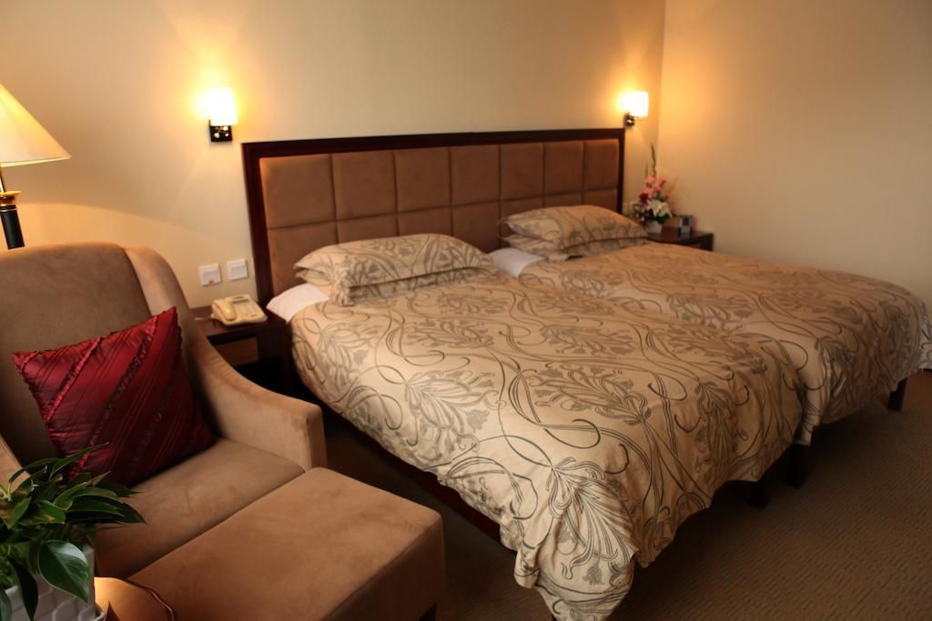 A hotel room with a bed, a chair, a bedside table, and a lamp.