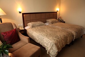 Una habitación de hotel con una cama, una silla, una mesita de noche y una lámpara.