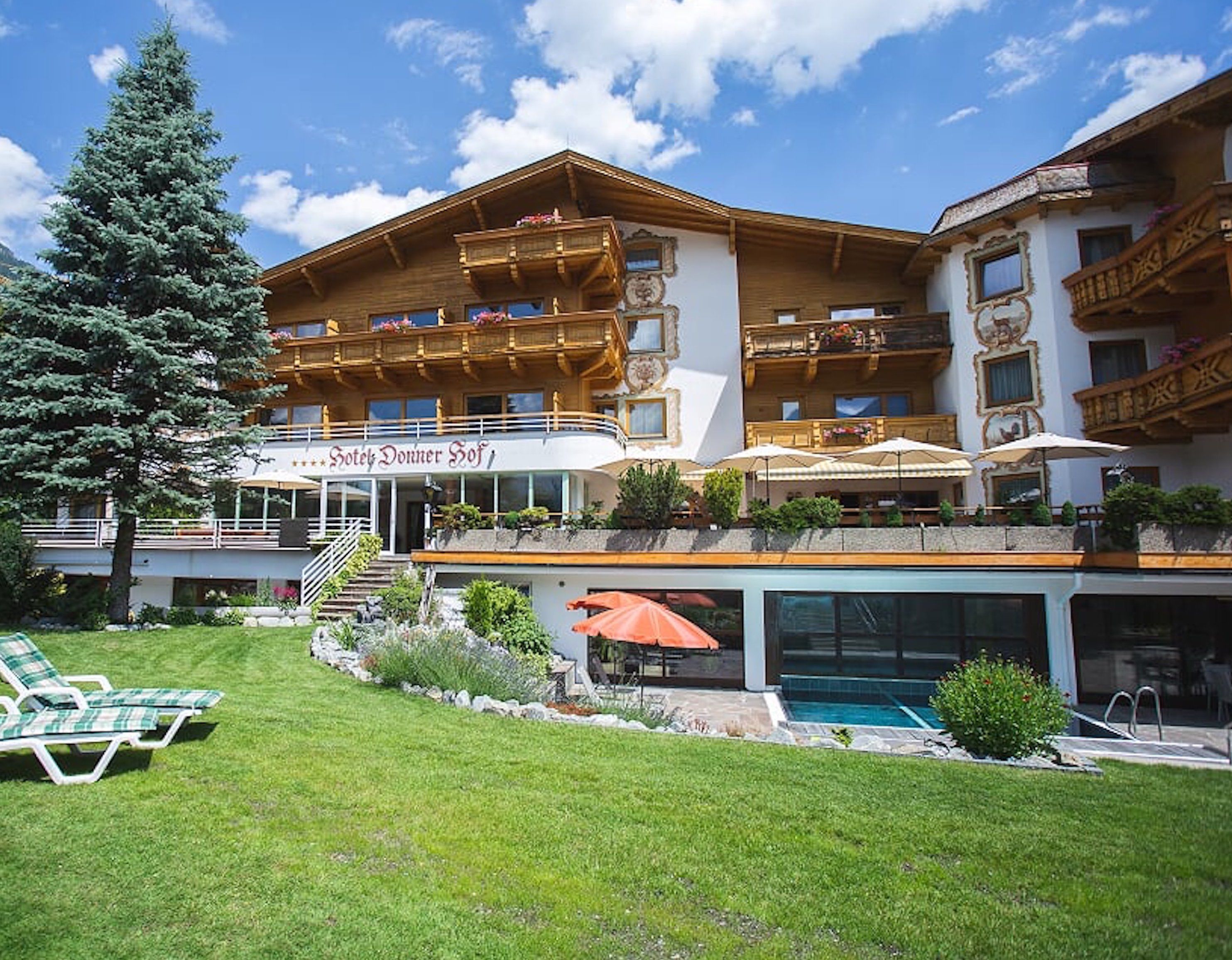 A hotel with a pool, outdoor seating, and a large tree.