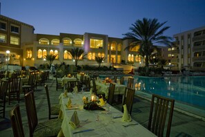 An outdoor dining area with tables set for guests, a pool, and a building with arched windows and balconies. - El Mouradi Tozeur (Tozeur)