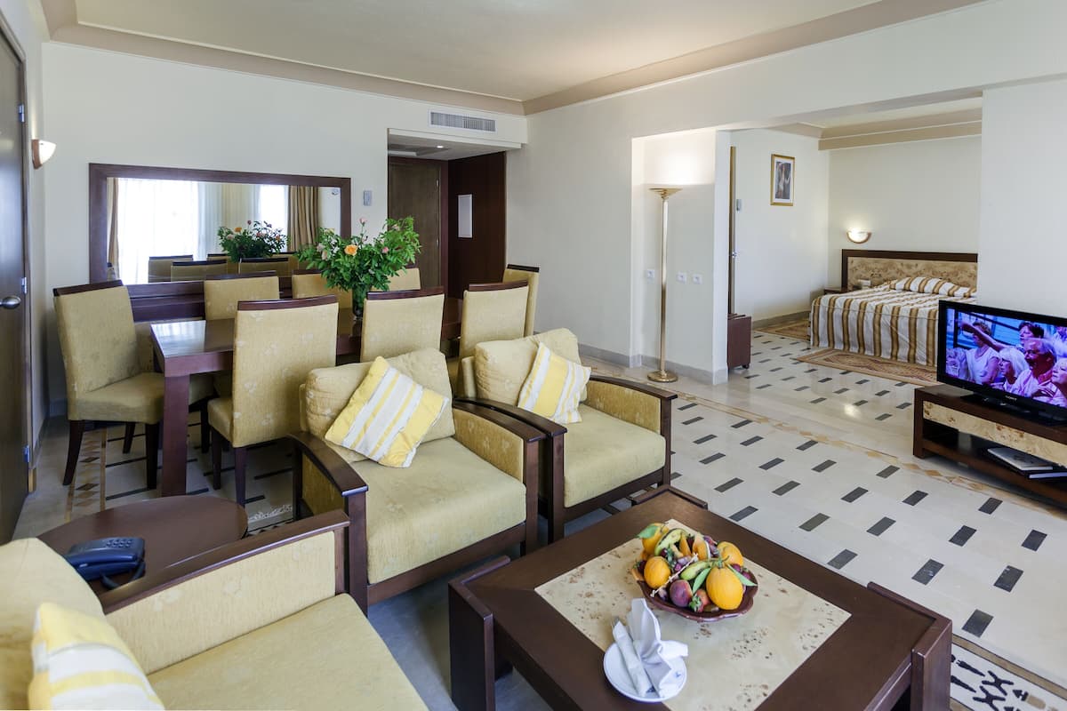 A hotel room with a dining area, a TV, and a fruit bowl on the coffee table.