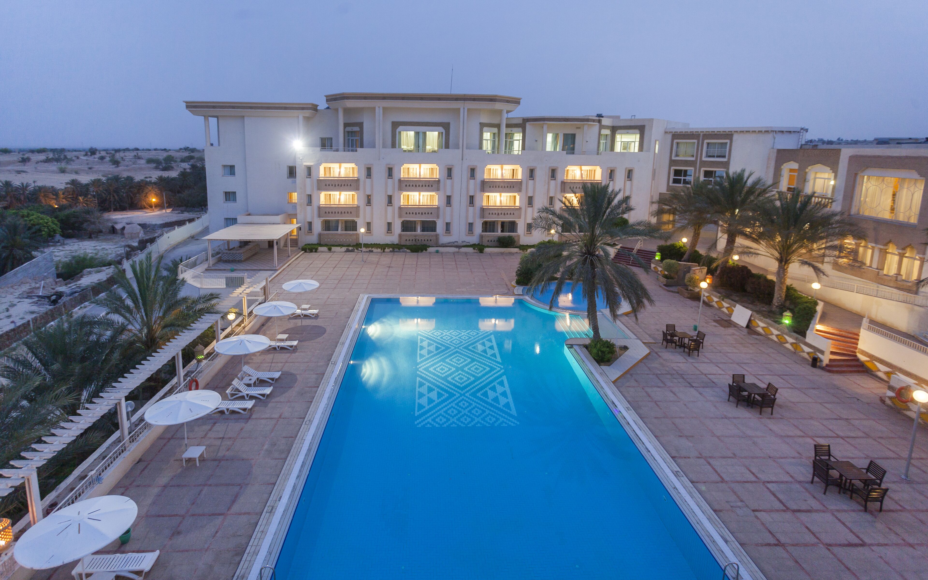 A hotel with a swimming pool, sun loungers, and a covered patio area.