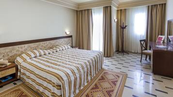 A hotel room with a bed, a desk, a chair, a rug, and curtains.