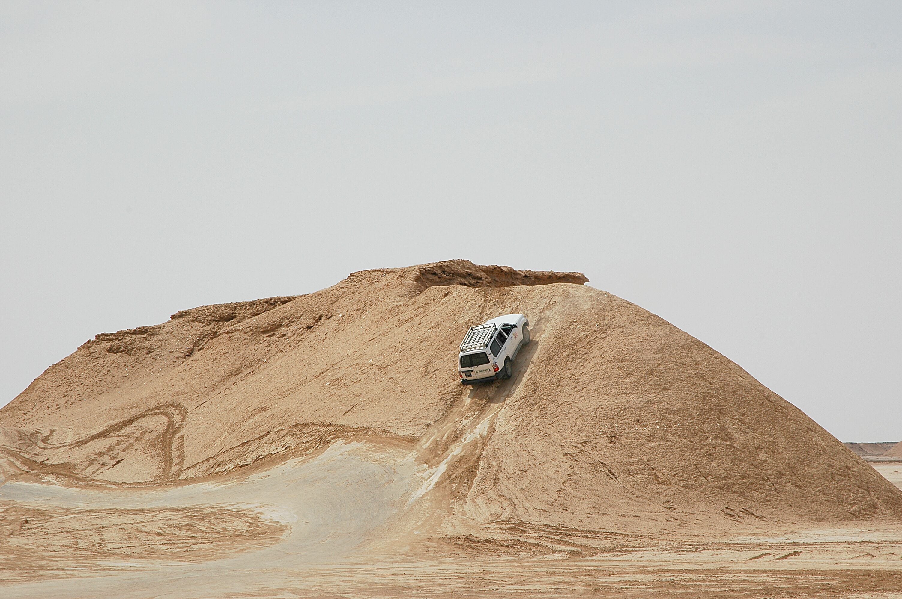 A white vehicle descending a large, sandy hill.