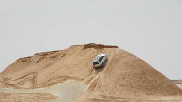 A white vehicle descending a large, sandy hill.