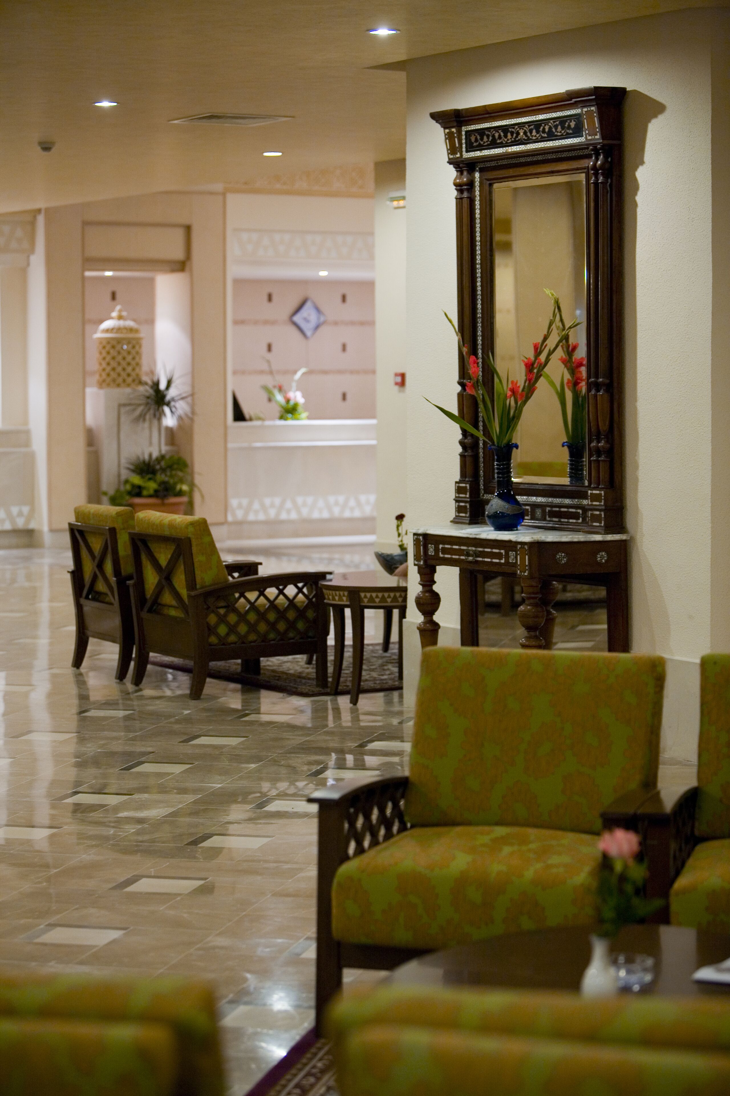 A lobby with a reception desk, chairs, a large mirror, and a vase with flowers.
