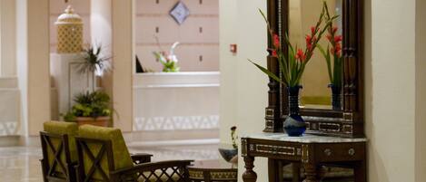 A lobby with a reception desk, chairs, a large mirror, and a vase with flowers.