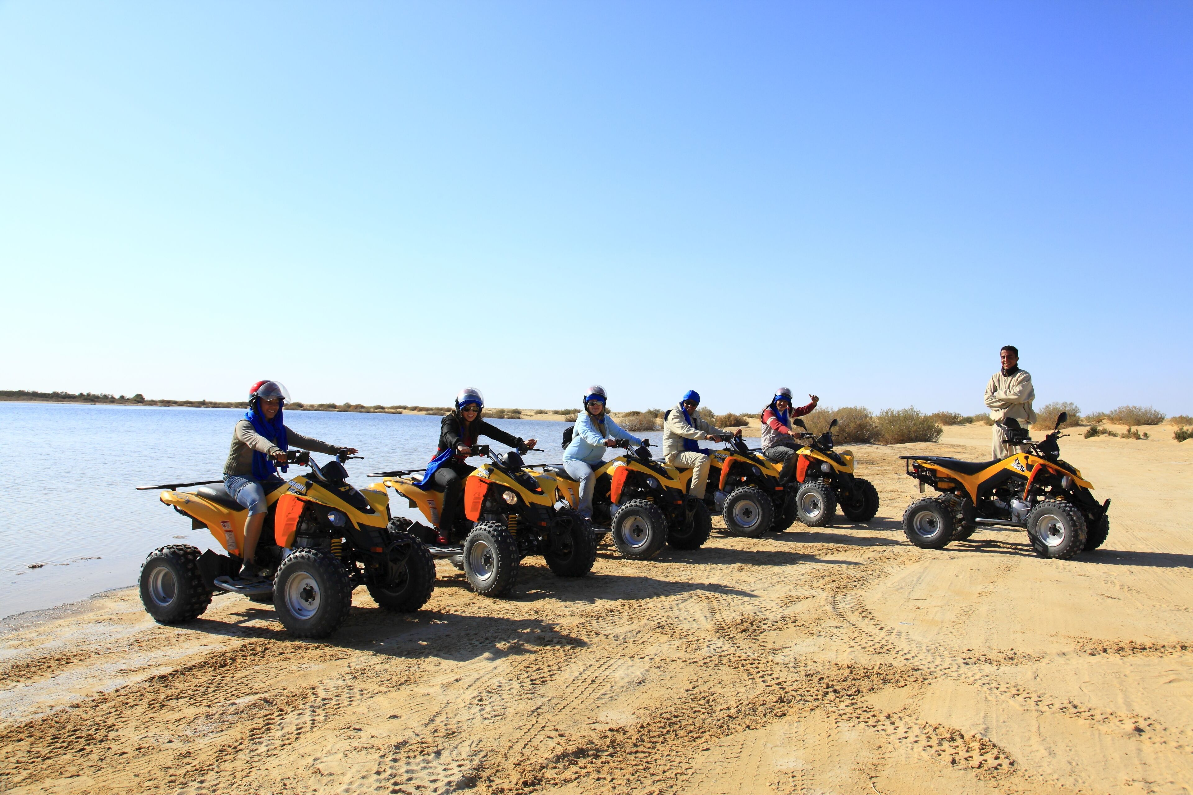 Un groupe de personnes sur des quads, sur une plage de sable près de l’eau.