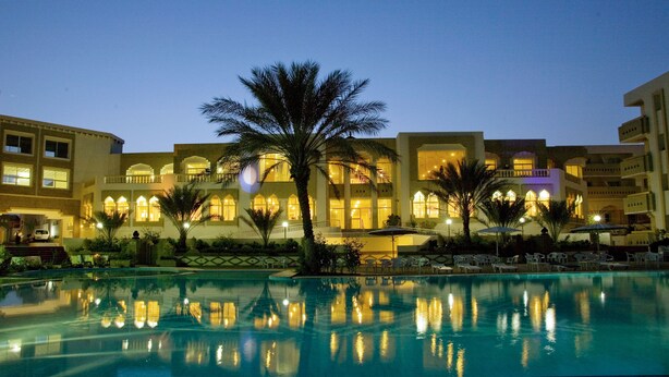 A hotel with a swimming pool, palm trees, and illuminated windows. - El Mouradi Tozeur (Tozeur)