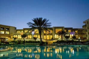 A hotel with a swimming pool, palm trees, and illuminated windows. - El Mouradi Tozeur (Tozeur)