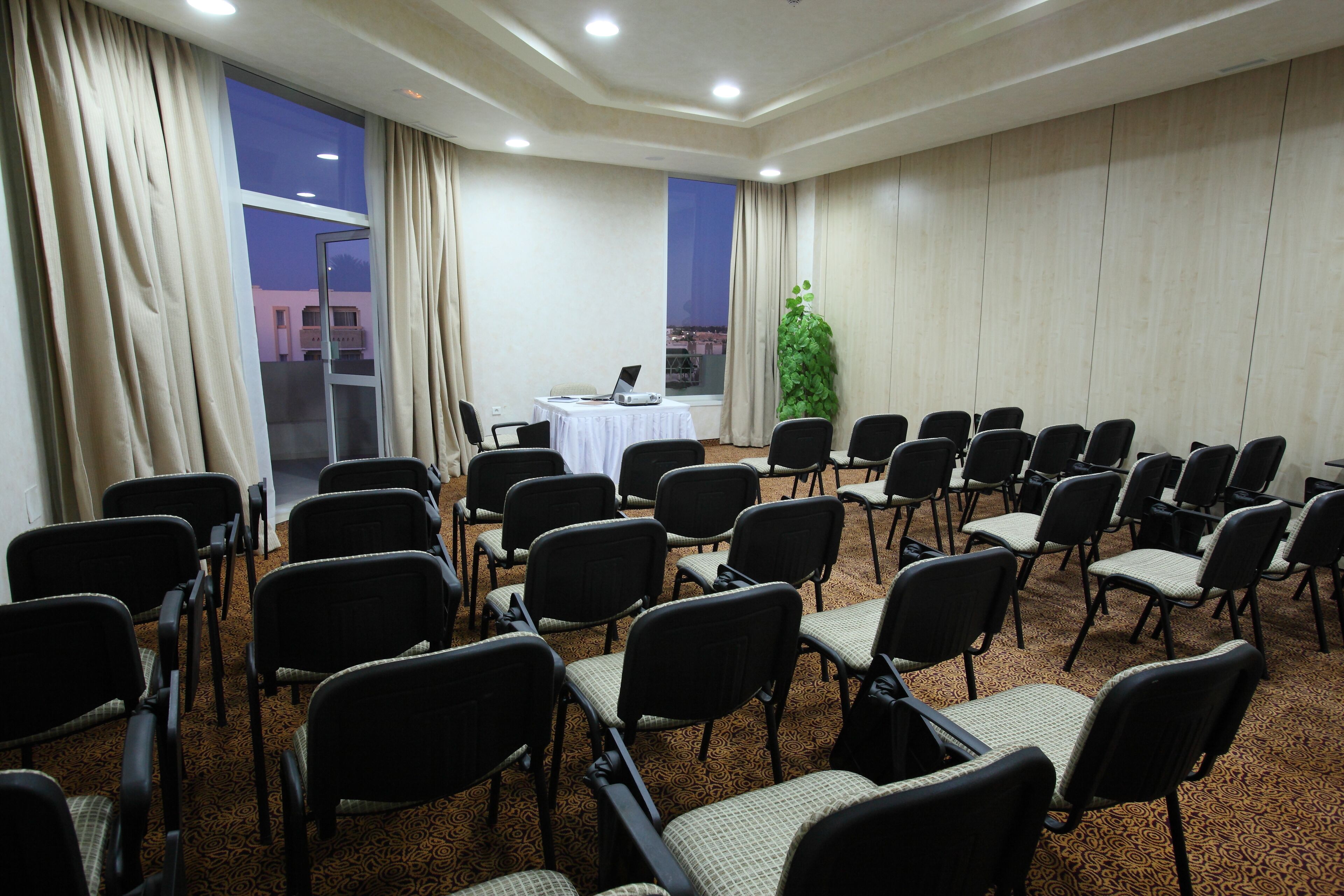 A conference room with rows of chairs, a laptop on a table, and a large window with curtains.