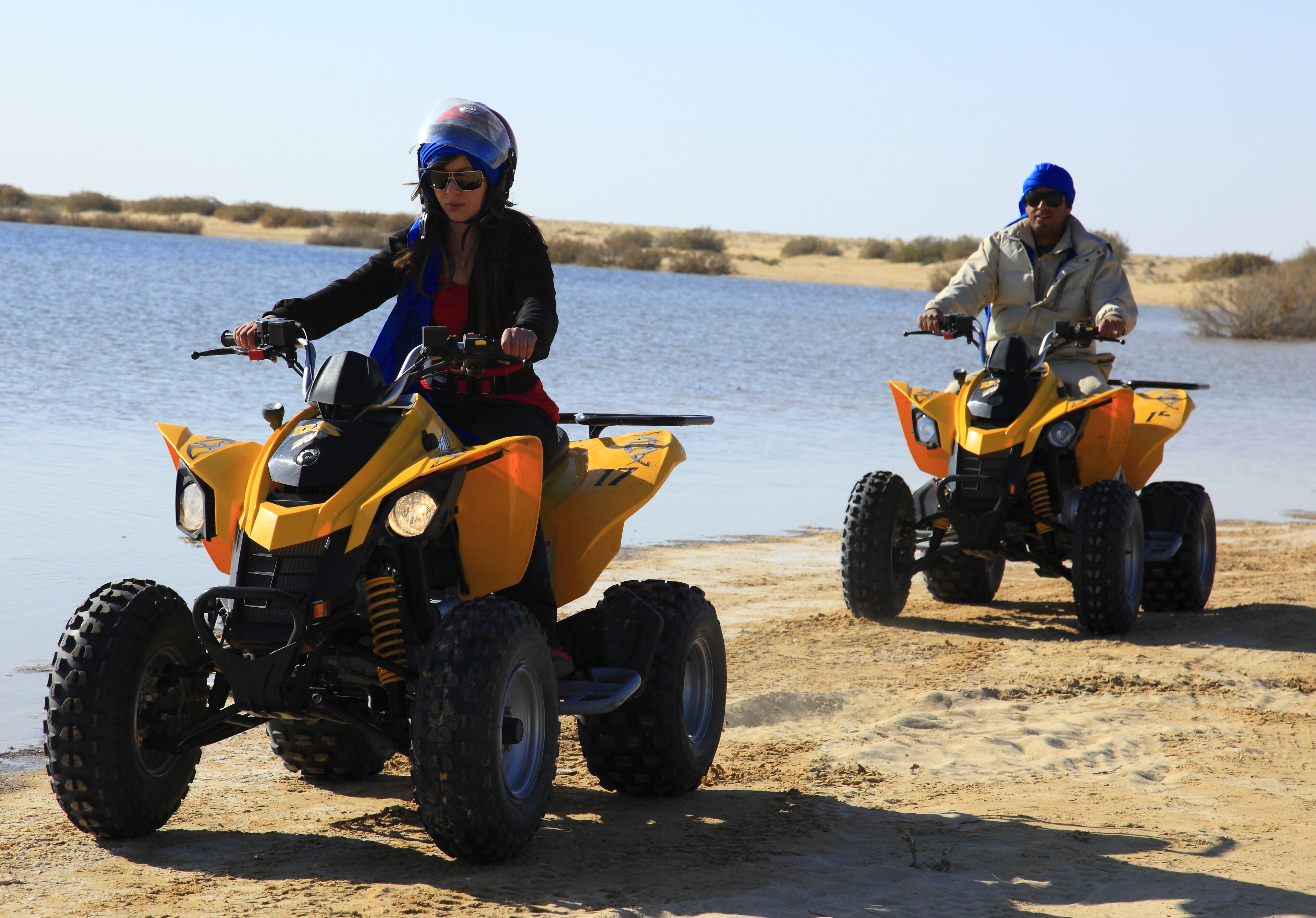 Two people riding ATVs on a sandy beach near water.