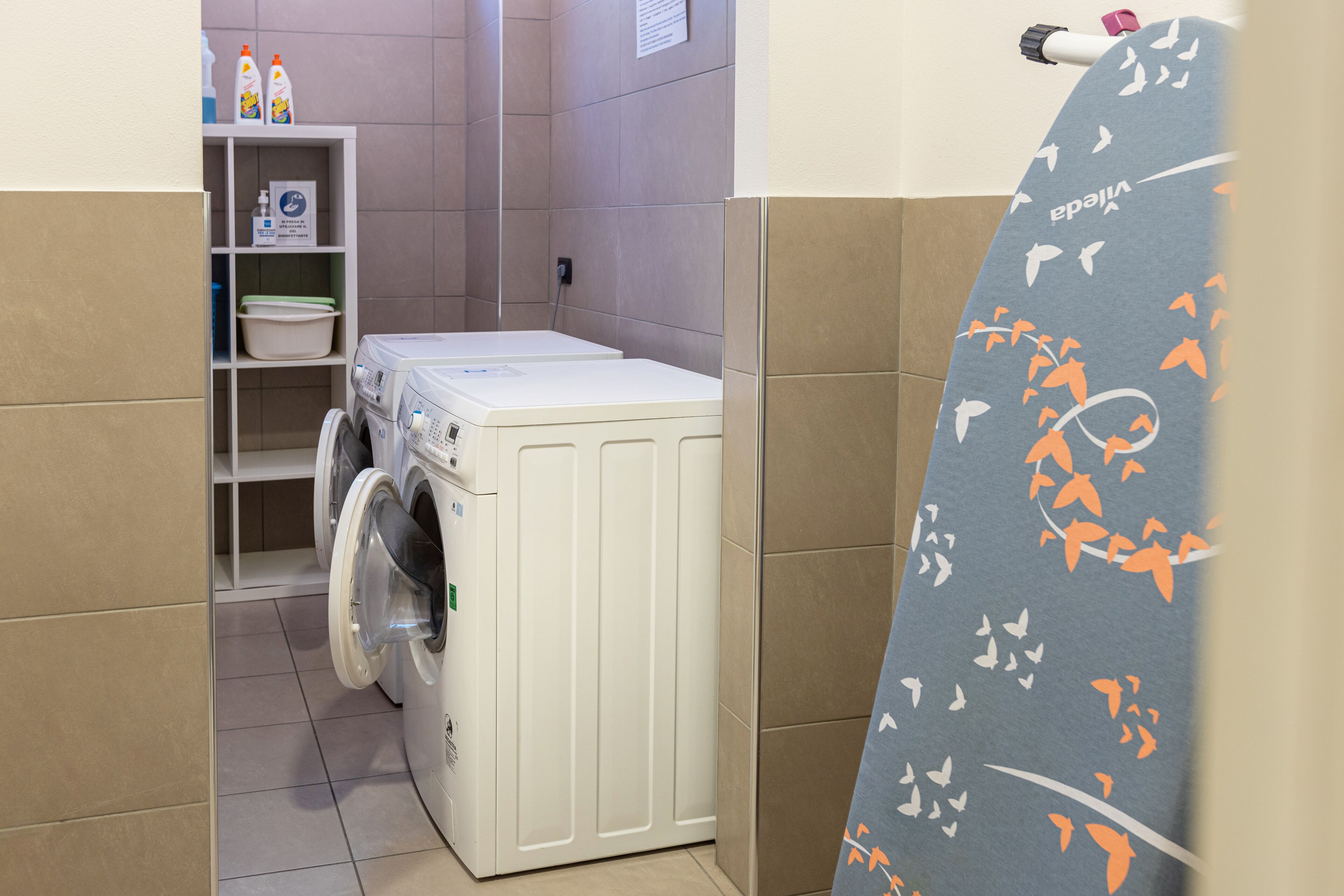 A laundry area with a washing machine, shelves with cleaning supplies, and a patterned shower curtain.