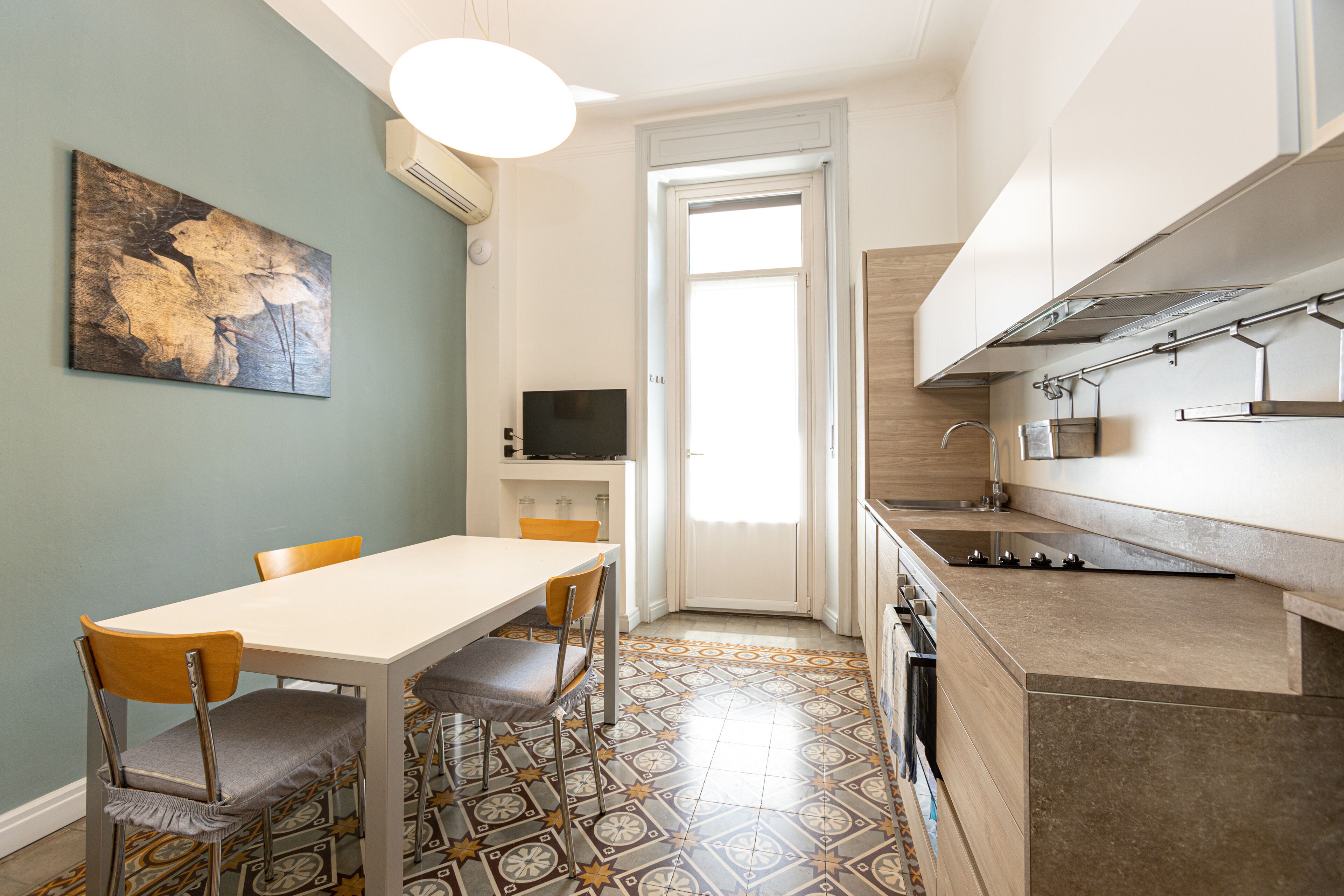 A compact kitchen with a dining area, a TV, and a large window.