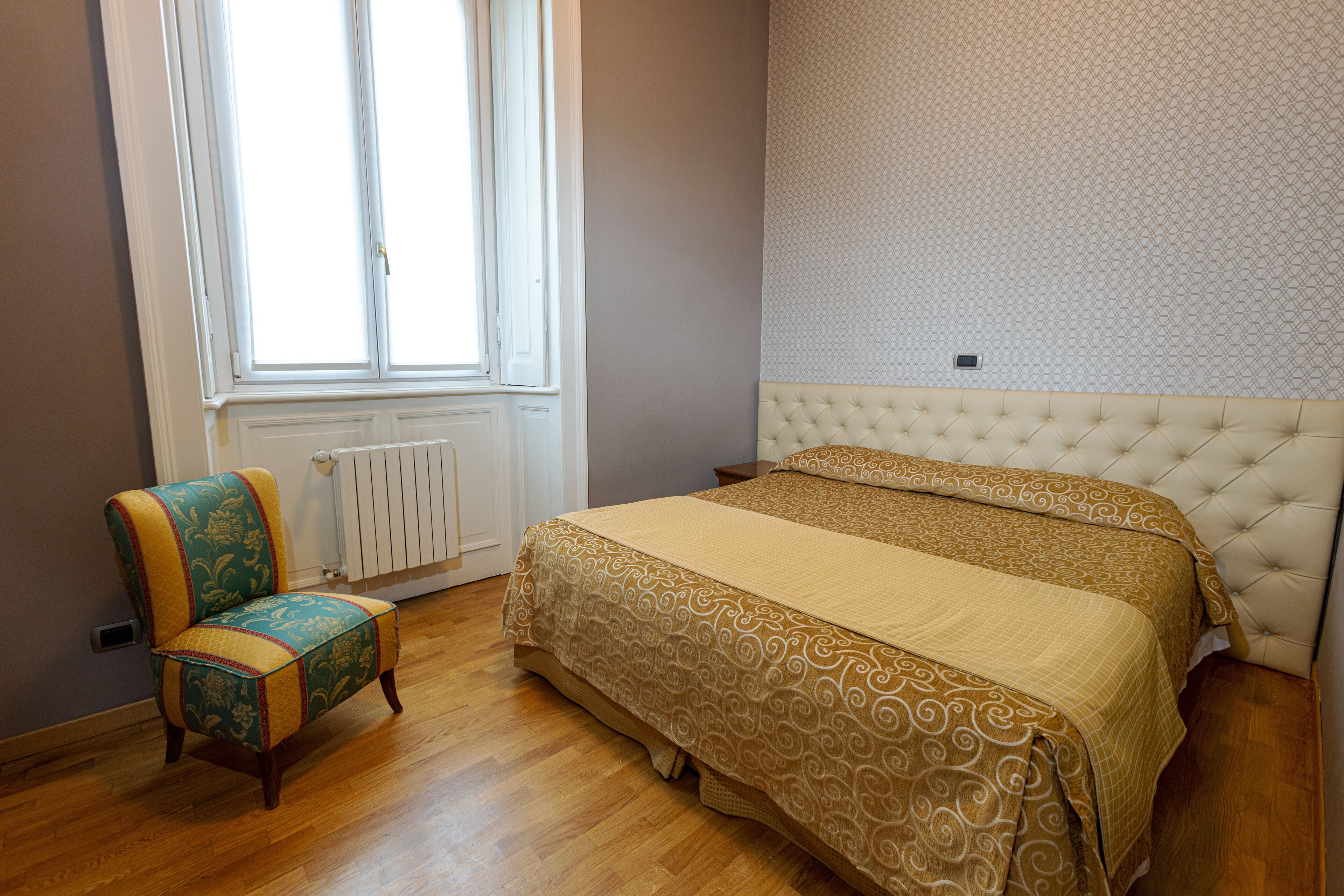 A bedroom with a bed, a chair, a radiator, and a window.