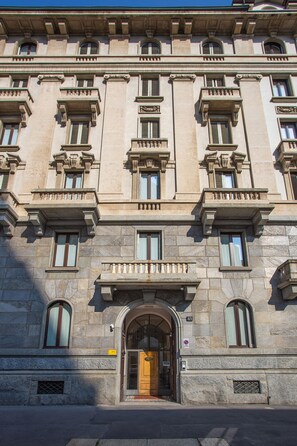 Un edificio histórico con una entrada imponente, múltiples ventanas y detalles arquitectónicos de estilo clásico.