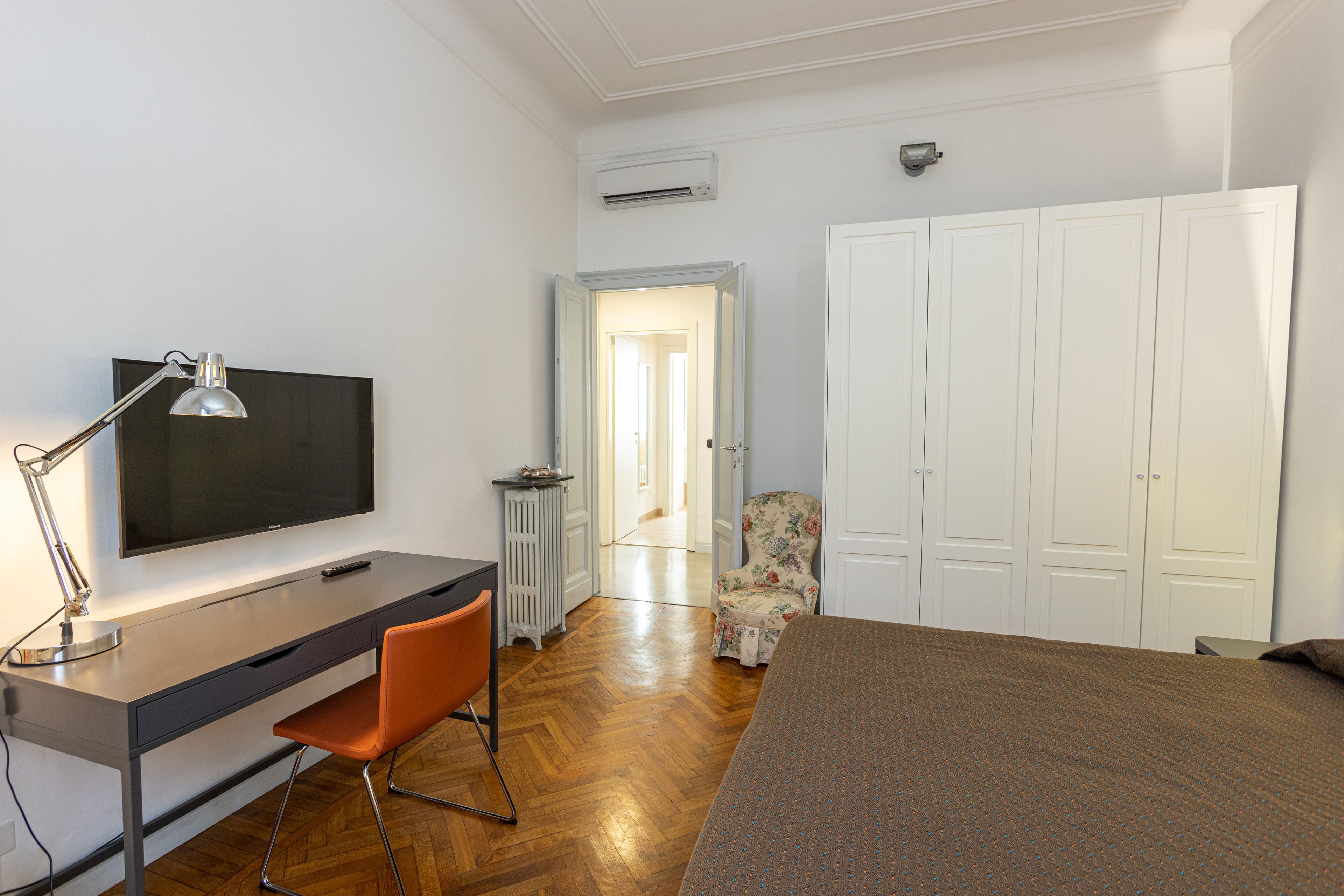 A bedroom with a bed, a desk with a chair, a TV, and a wardrobe.