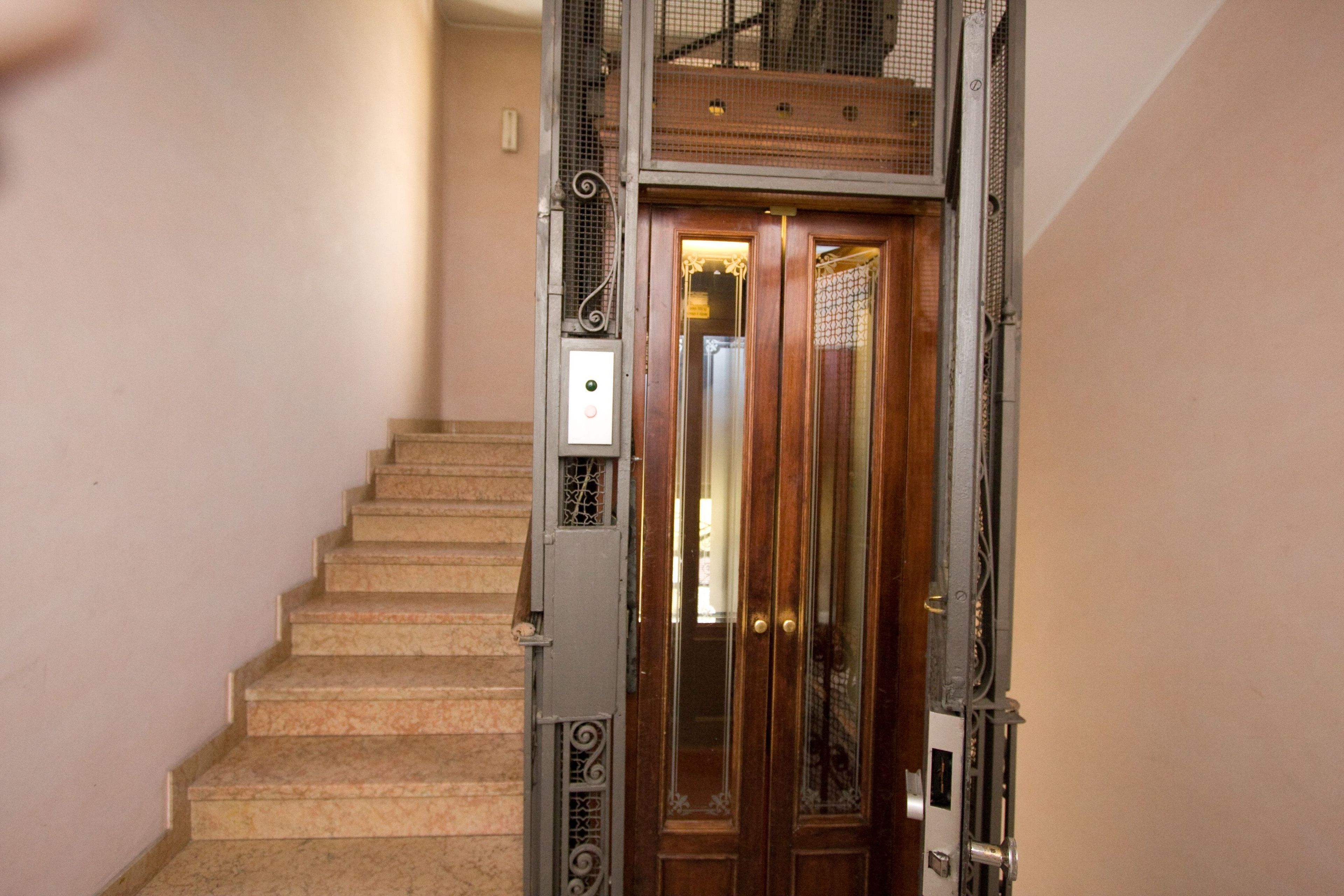 A staircase with a wooden door at the top, a metal railing, and a control panel.