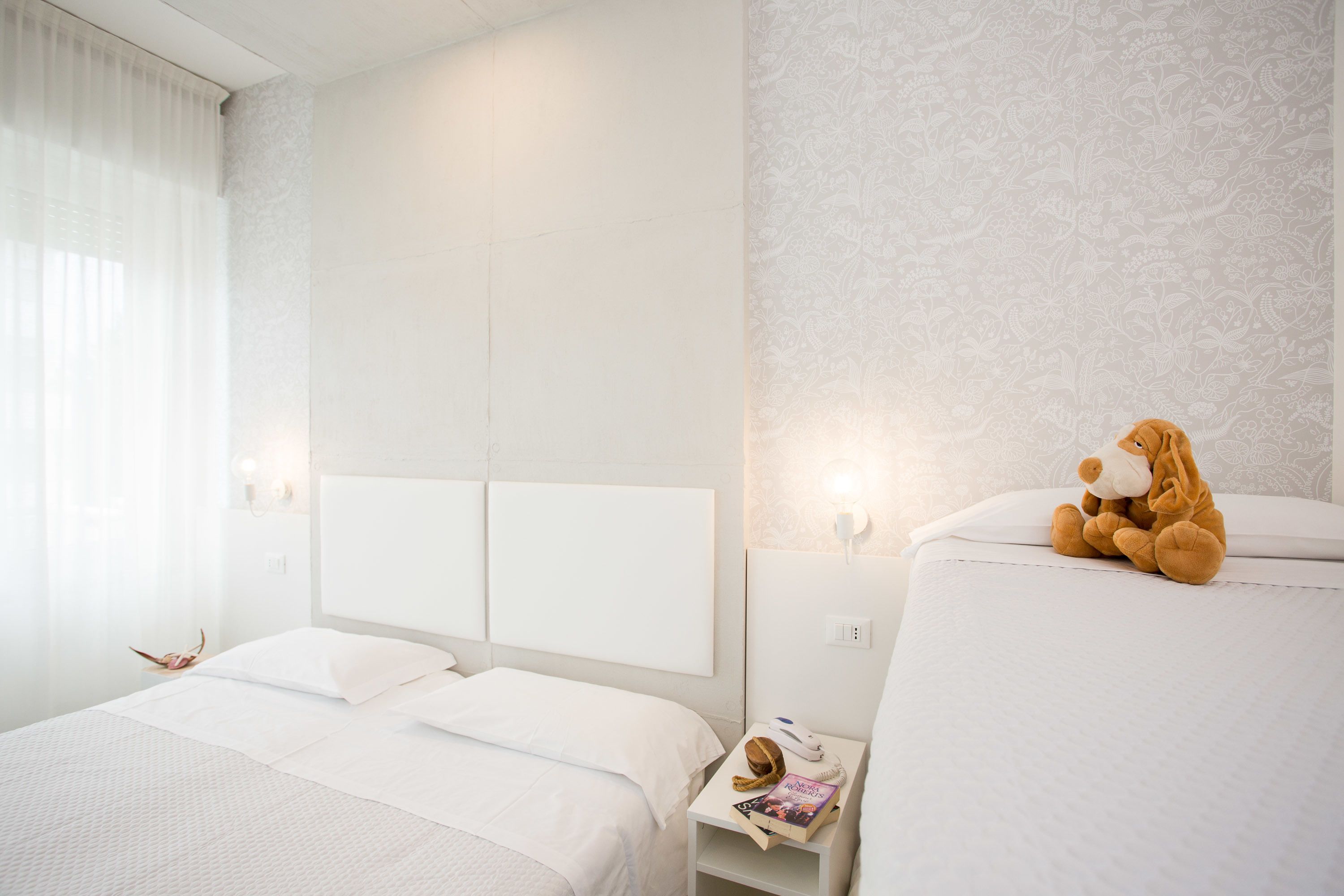 A hotel room with two beds, a nightstand with a lamp, and a plush toy on the right bed.