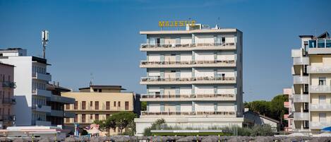 A multi-story hotel with balconies, located near a beach with sun loungers and umbrellas.