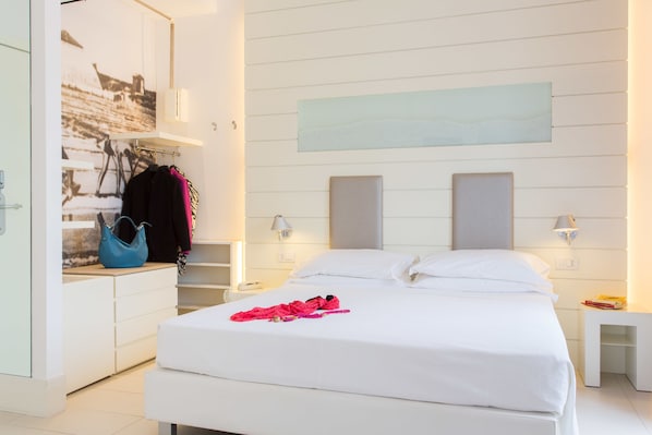 A modern hotel room with a large bed, bedside tables, a wardrobe, and a wall-mounted artwork. - Majestic (Cervia)