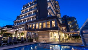 A multi-story hotel with balconies, a swimming pool, and outdoor seating areas. - Majestic (Cervia)