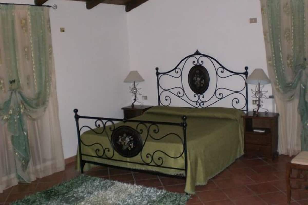 A bedroom with a bed, two nightstands, a lamp on each nightstand, and a window with curtains.