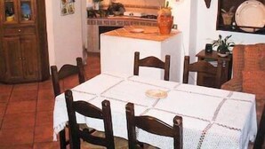 Ein gemütlicher Essbereich mit einem Tisch, gedeckt für vier Personen, umgeben von Holzstühlen. Im Hintergrund ist eine Küche erkennbar, über der Arbeitsfläche hängt eine Leuchte.