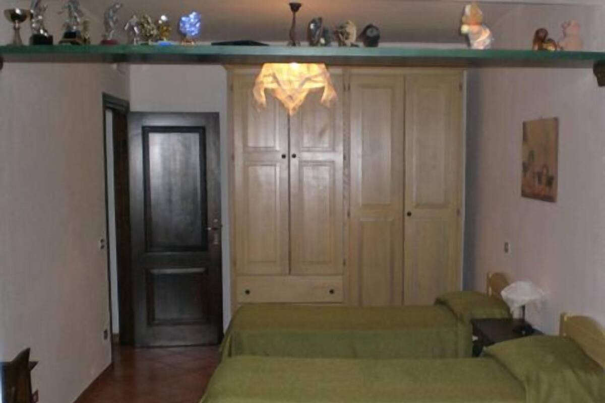 A bedroom with two beds, a wooden wardrobe, and a shelf with trophies.