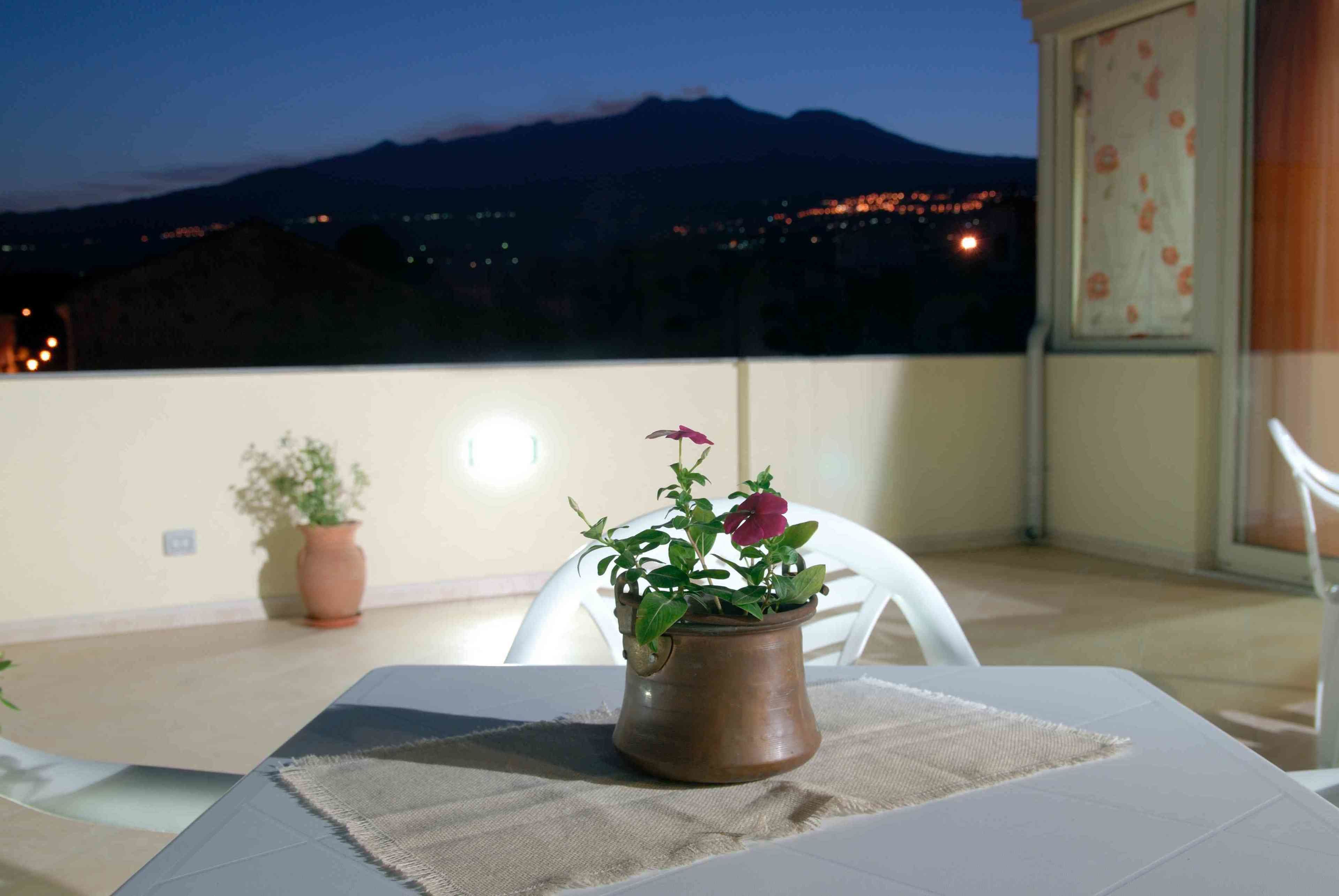A balcony with a table, a potted plant, and a view of a mountain at dusk.