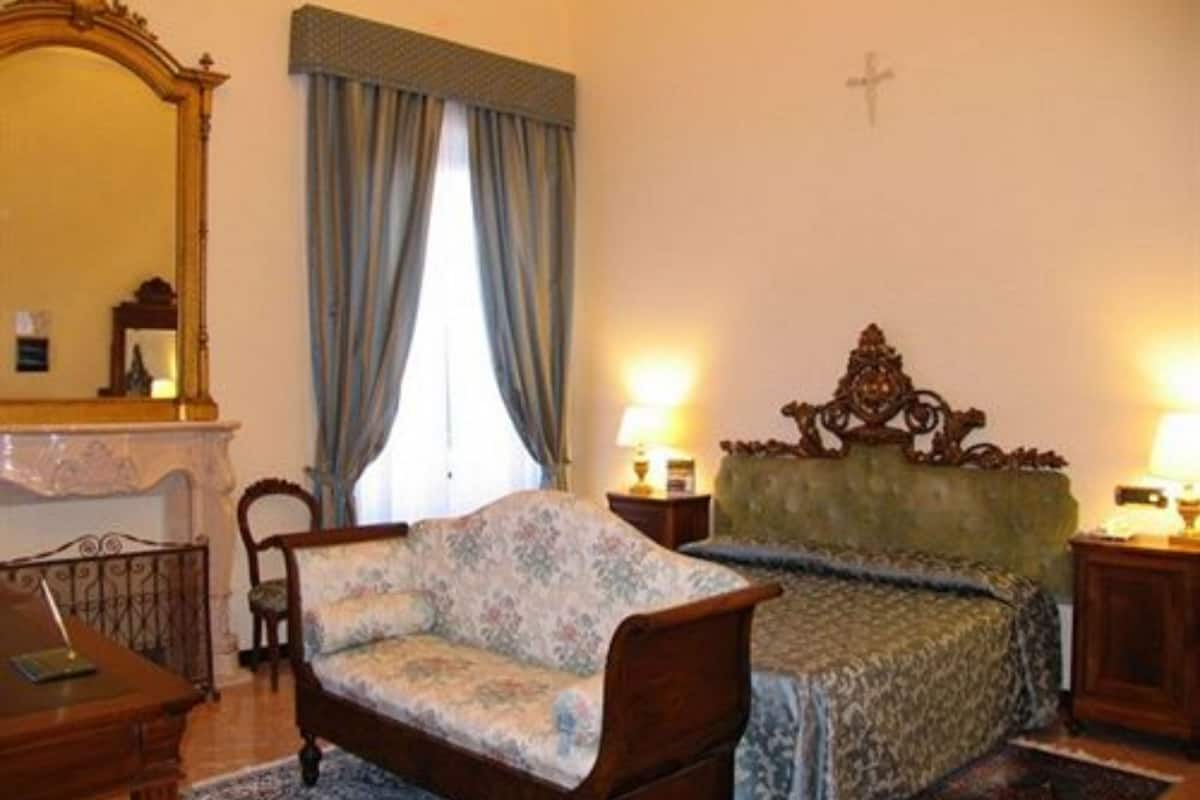 Une chambre avec un canapé à motifs floraux, un lit avec une tête de lit verte, une commode en bois et un grand miroir.
