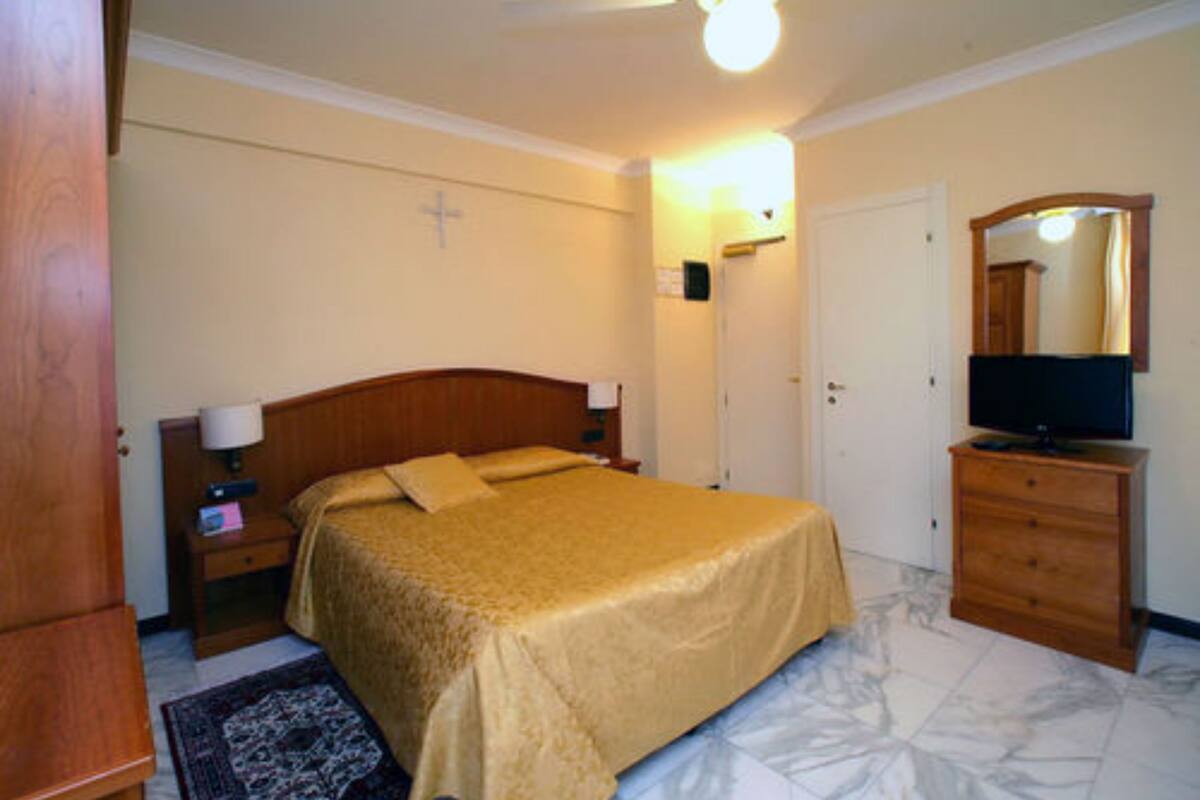 Une chambre à coucher avec un lit, une table de chevet, une commode, un téléviseur et un crucifix au mur.
