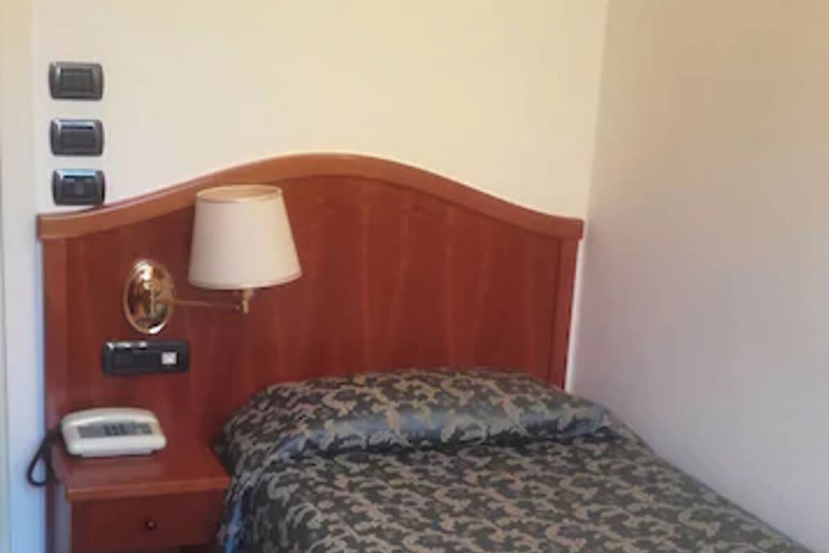 Une chambre d’hôtel avec une tête de lit en bois, une table de chevet avec une lampe, un téléphone et une couvre-lit à motifs.
