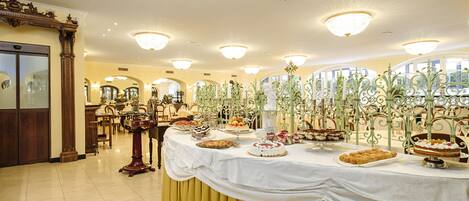 A banquet hall with a long table covered in various desserts and a chandelier.