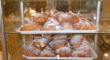 A display case with pastries, including croissants and other baked goods, dusted with powdered sugar.
