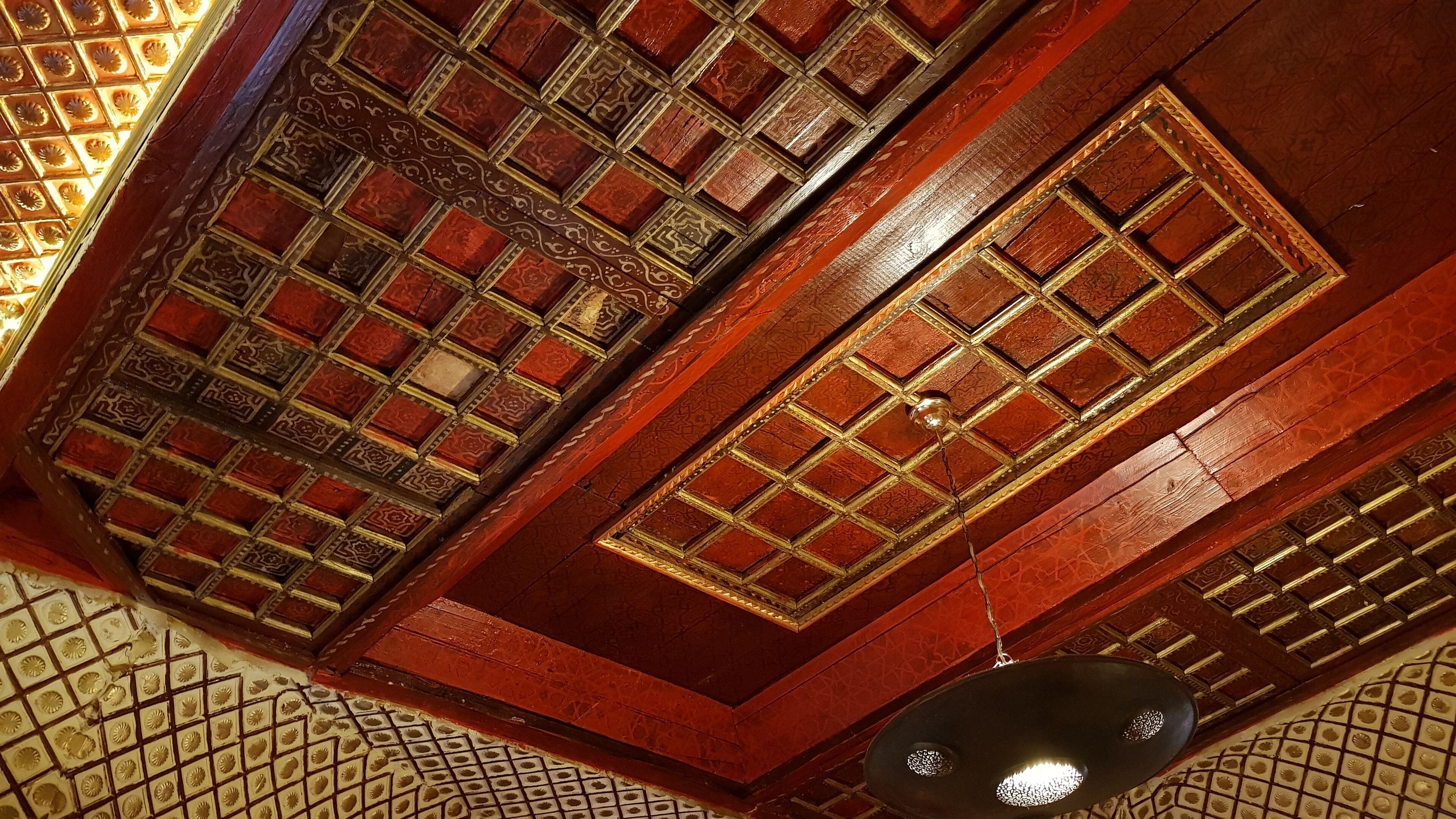 A ceiling with intricate geometric patterns and a hanging light fixture.