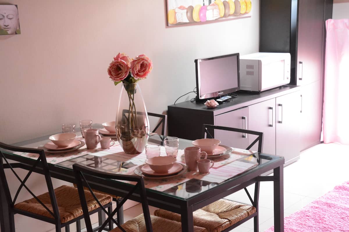 A dining area with a glass table set for four, surrounded by wicker chairs. A vase with pink flowers is on the table.