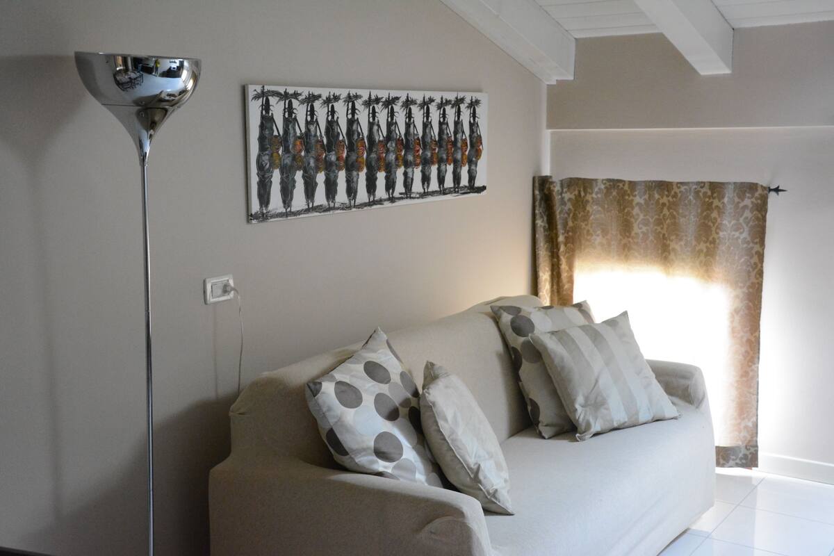 A living room with a sofa, patterned cushions, a floor lamp, and a wall painting.