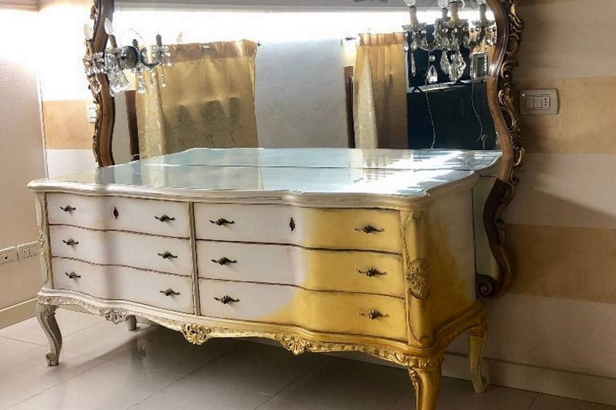 A vintage dresser with a large mirror, multiple drawers, and ornate gold detailing.