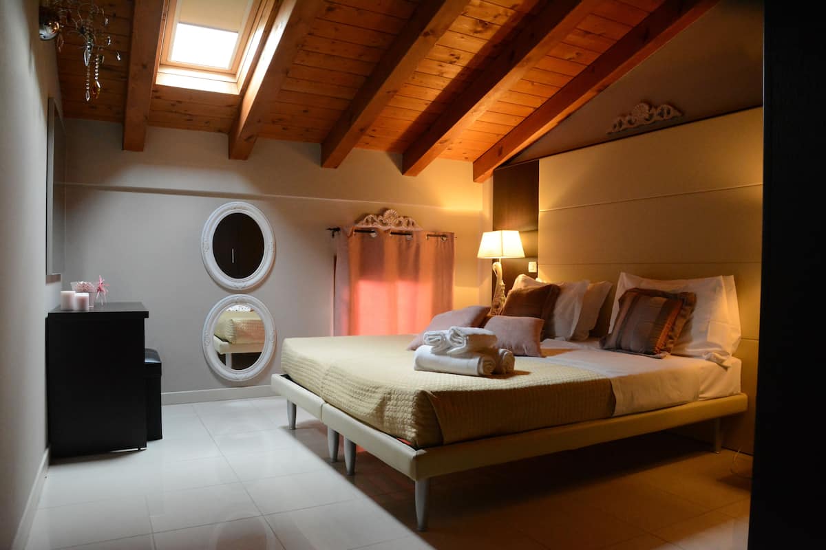 A bedroom with a bed, bedside table, mirror, and a skylight.
