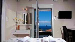 A hotel room with a bed, a desk, a mirror, a vase with flowers, and a view of the sea. - Brentanos Apartments ~ A ~ View of Paradise (Corfu)