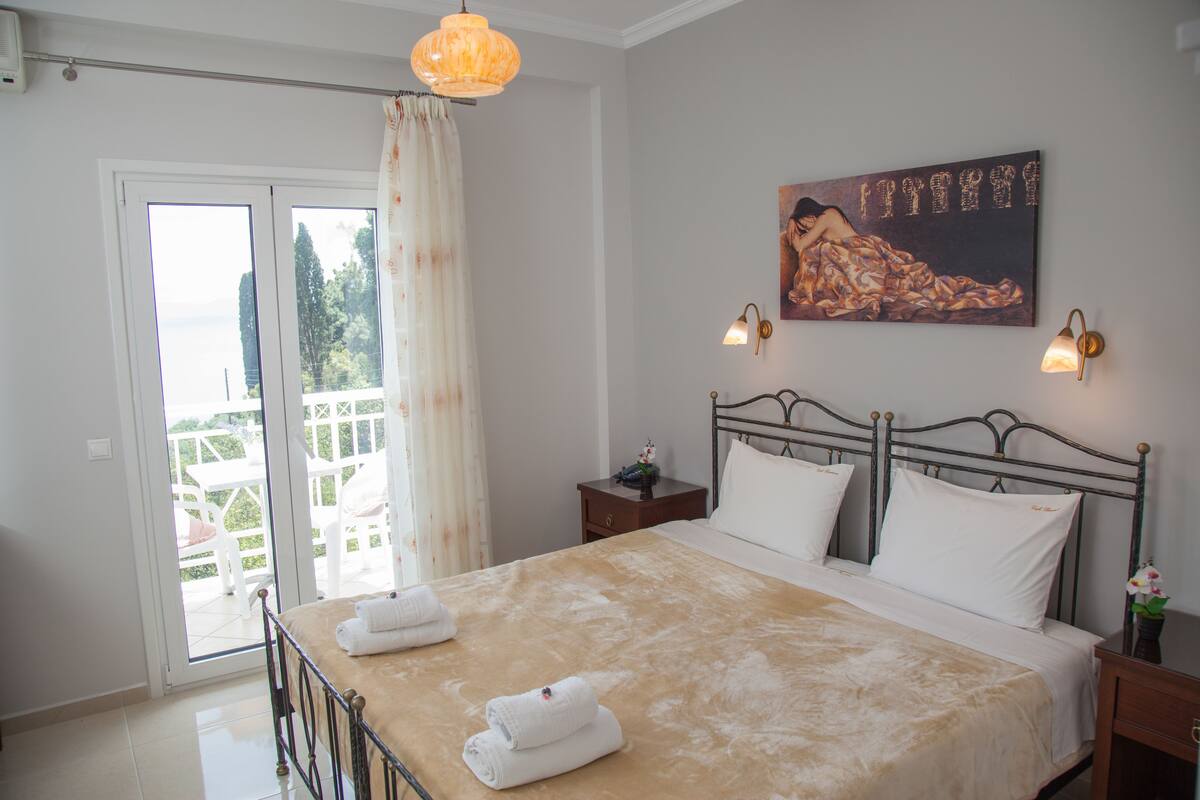 A bedroom with a bed, a nightstand, a painting, and a view through the glass doors.