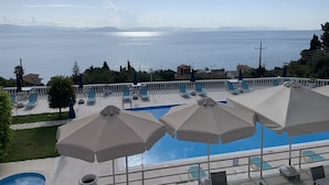 A poolside area with lounge chairs and umbrellas, overlooking a body of water and distant mountains. - Brentanos Apartments ~ A ~ View of Paradise (Corfu)