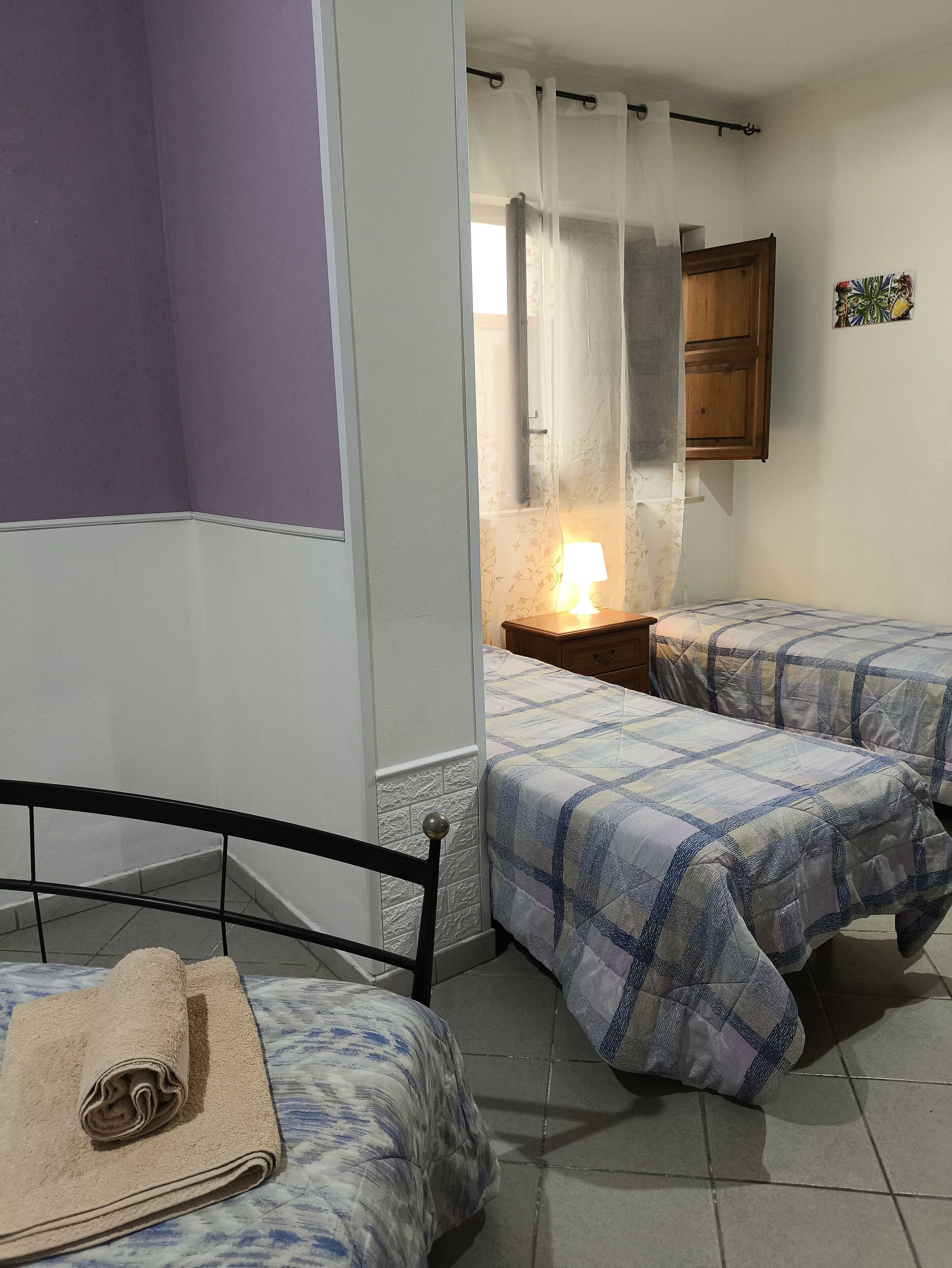 A bedroom with two beds, a nightstand with a lamp, a wooden cabinet, and a window with curtains.