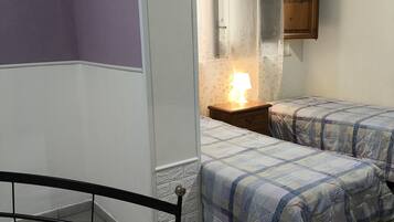 A bedroom with two beds, a nightstand with a lamp, a wooden cabinet, and a window with curtains.